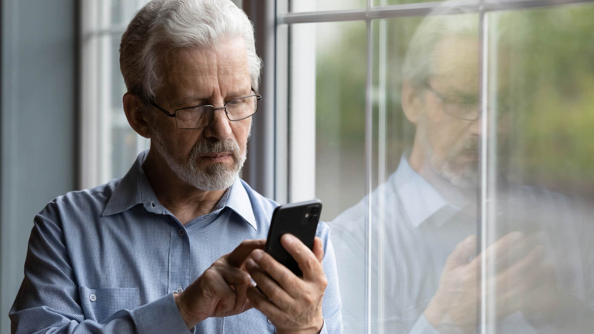 older man looking sad staring at his phone waiting for a text or call